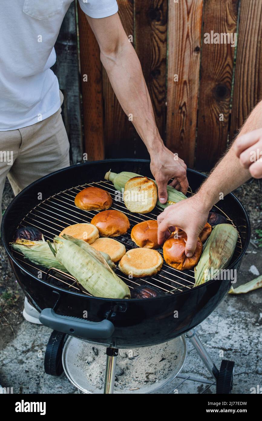 Zwei Jungs, die im Sommer Hamburgerbrötchen und Mais auf dem Maiskolben feilschen Stockfoto