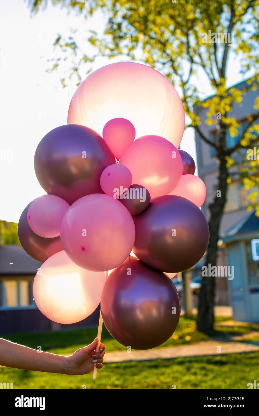 Zusammensetzung aus weißen, rosa, transparenten Heliumballons in der Hand einer Frau auf einem Außenhintergrund. Stockfoto