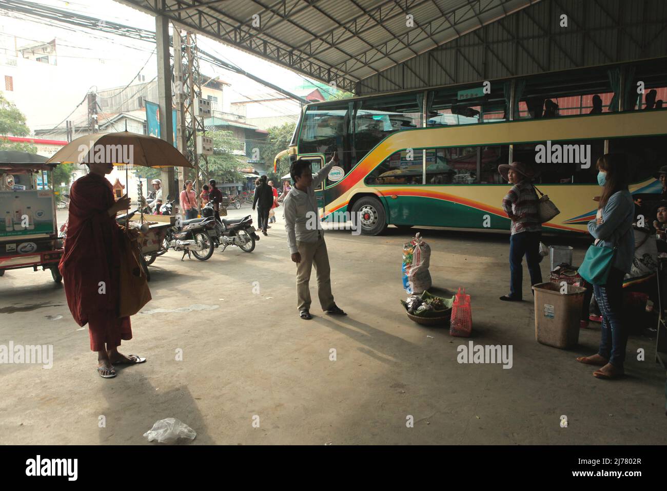 Ein buddhistischer Mönch, der einen Regenschirm trägt, während er während einer morgendlichen Almosenrunde an einer Intercity-Bushaltestelle in Phnom Penh, Kambodscha, steht. Stockfoto