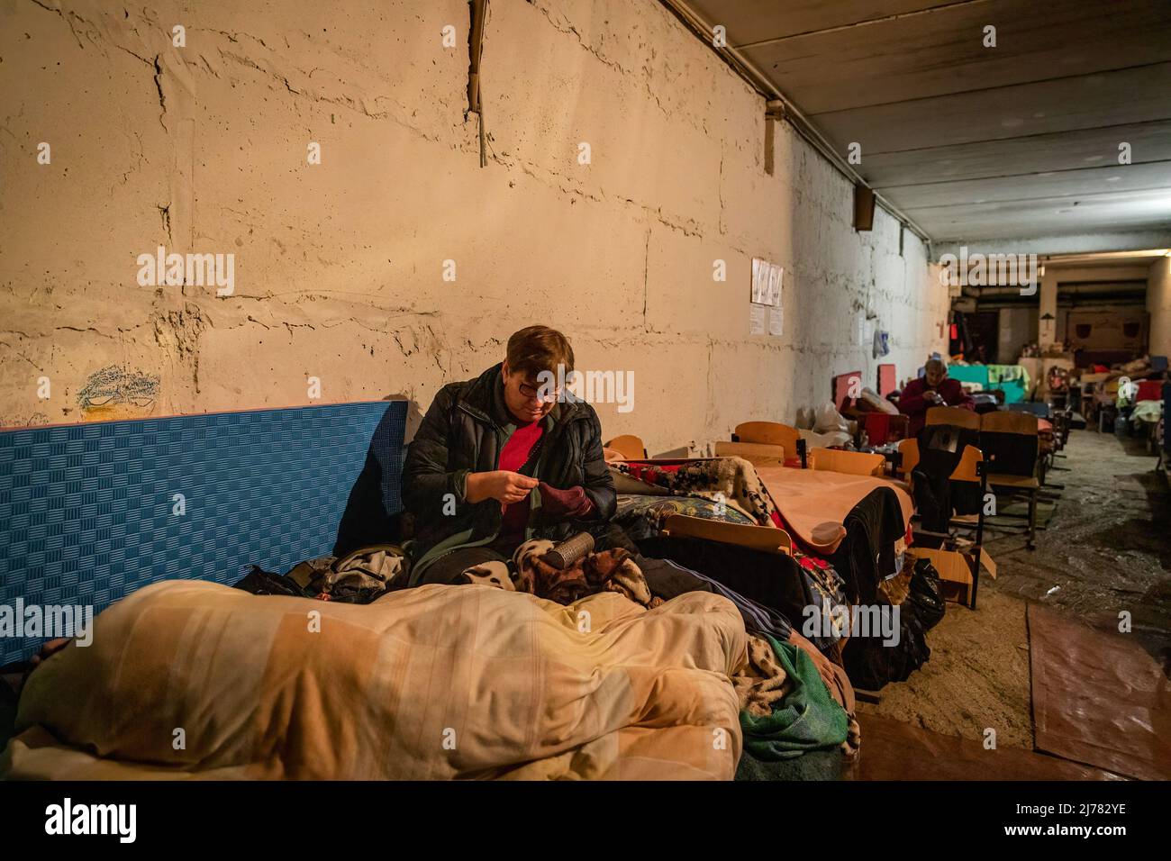 28. April 2022, Kharkiv, Kharkiv'ka Oblast''', Ukraine: Eine Frau strickt sich an, als ihr Mann neben ihr in einem unterirdischen Bunker einer Schule im Südosten von Kharkiv schläft, in der jetzt etwa 100 Zivilisten, darunter Kinder, leben. Die Bürger in Charkiw wurden gezwungen, ein neues Leben im Untergrund in Bunkern ohne Strom und Wasser zu übernehmen, da die zweitgrößte Stadt in der Ukraine nun ständig von russischen Bombardierungen und Luftangriffen bedroht ist. Die Bürger in Charkiw wurden gezwungen, ein neues Leben im Untergrund in Bunkern ohne Strom und Wasser zu adoptieren. Die zweitgrößte Stadt in der Ukraine jetzt Stockfoto