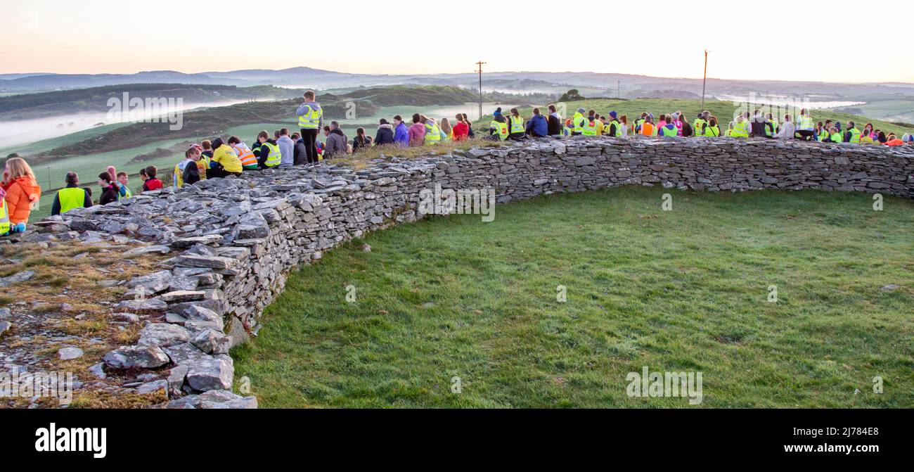 Menschenmengen beobachten den Sonnenaufgang nach der Dunkelheit in das Licht. Knockdrum Steinring Fort, West Cork, Irland Stockfoto