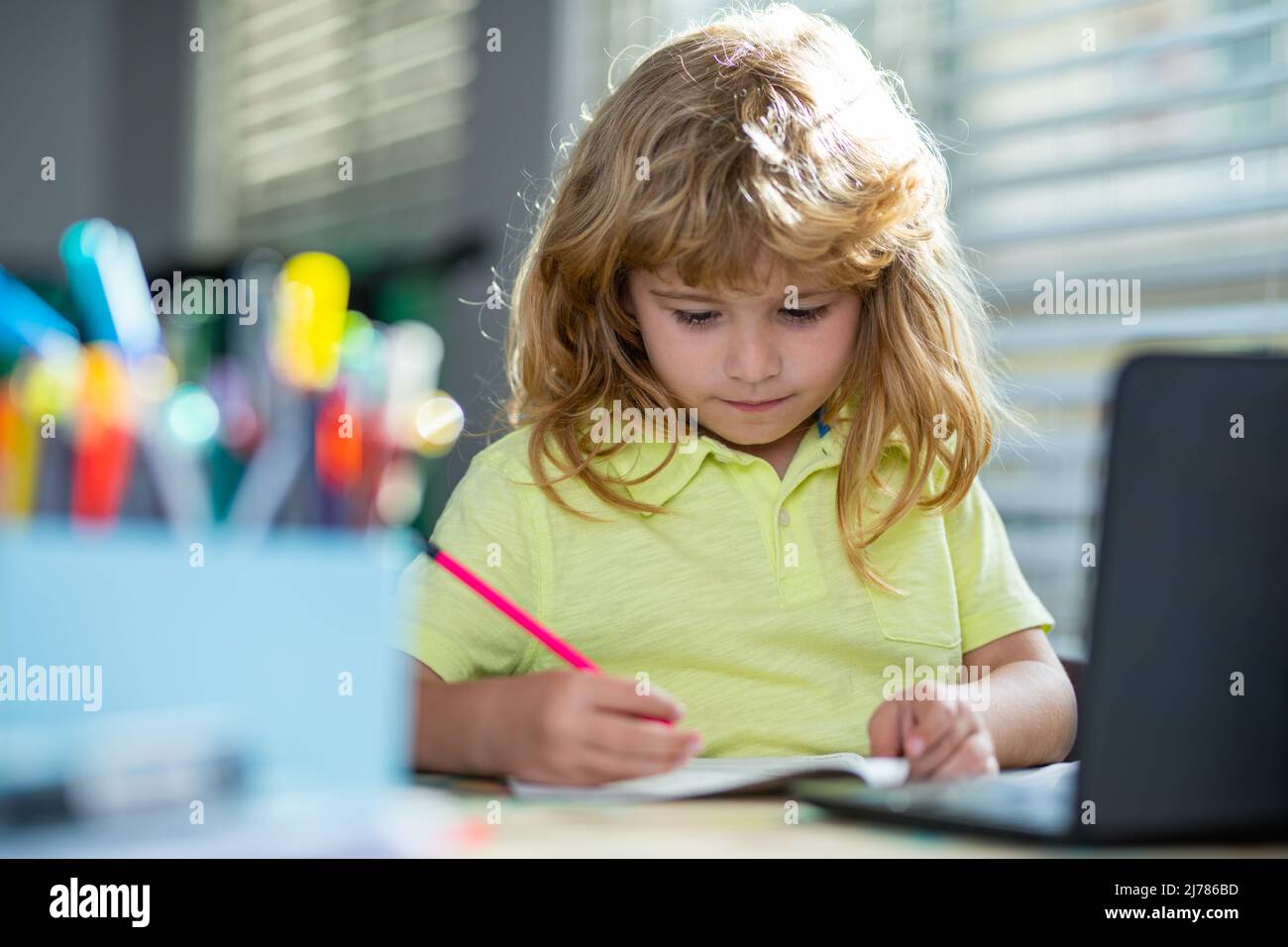 Kind schreibt Hausaufgaben in der Schulklasse. Ein Junge im Schulalter macht zu Hause Hausaufgaben. Porträt eines kleinen Schuljungen, der am Tisch sitzt und Hausaufgaben macht. Intelligent Stockfoto