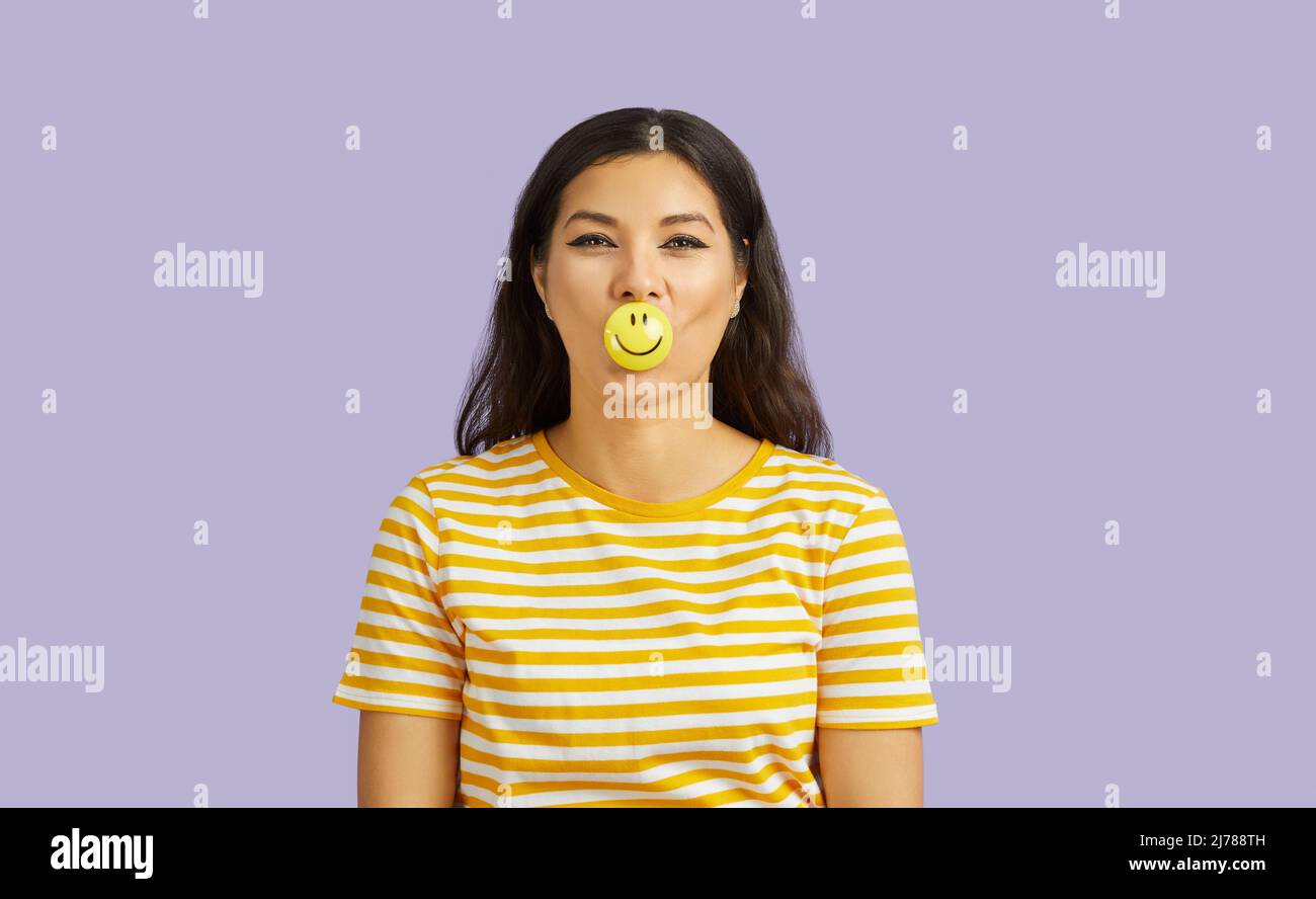 Fröhlich lächelnde junge Frau mit positiven Emoji auf Lippen isoliert auf pastellviolettem Hintergrund. Stockfoto