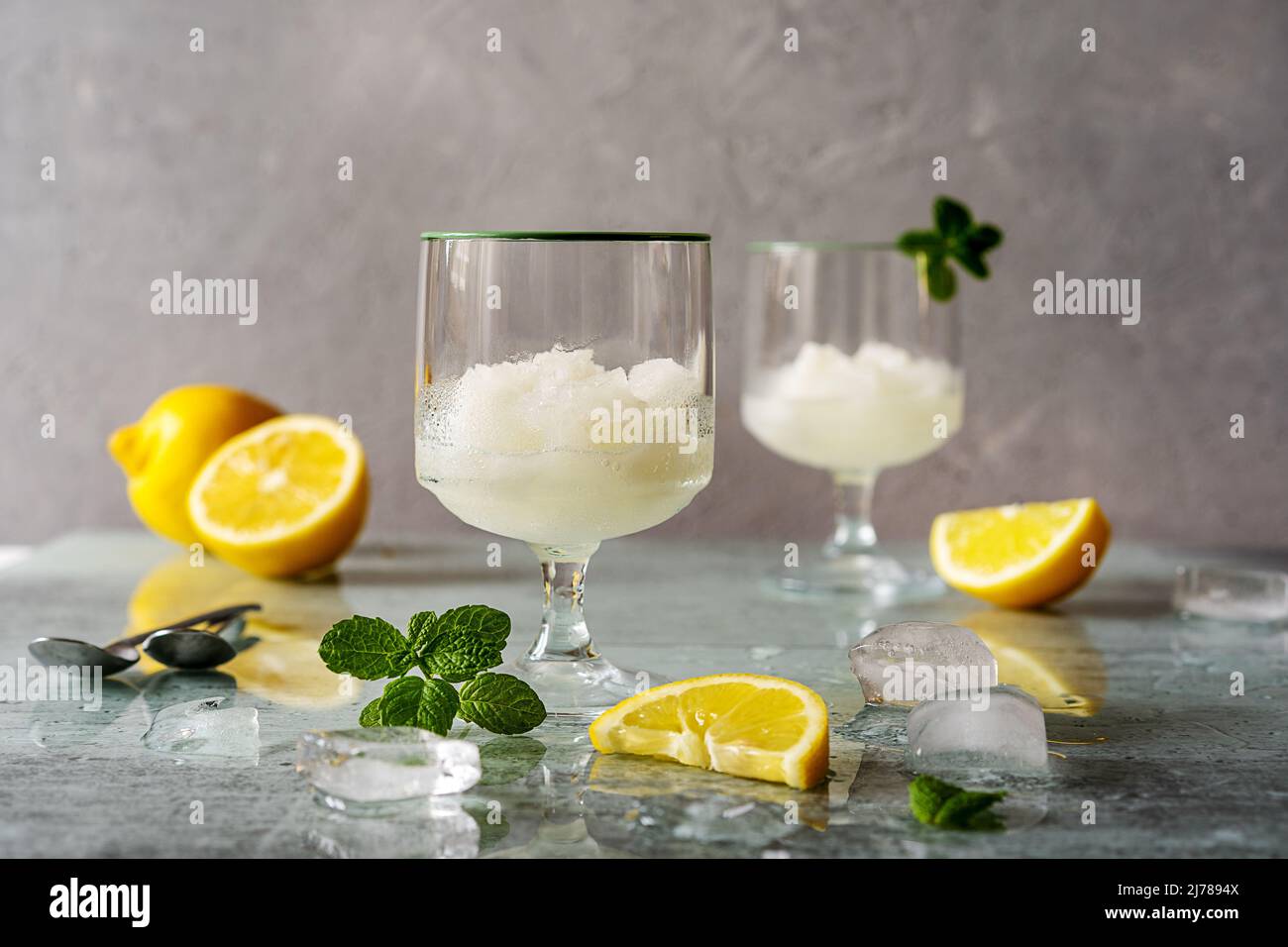 Zitronensorbet in zwei Gläsern mit Zitronen, Eiswürfeln, Minzblättern auf grauem Hintergrund Stockfoto