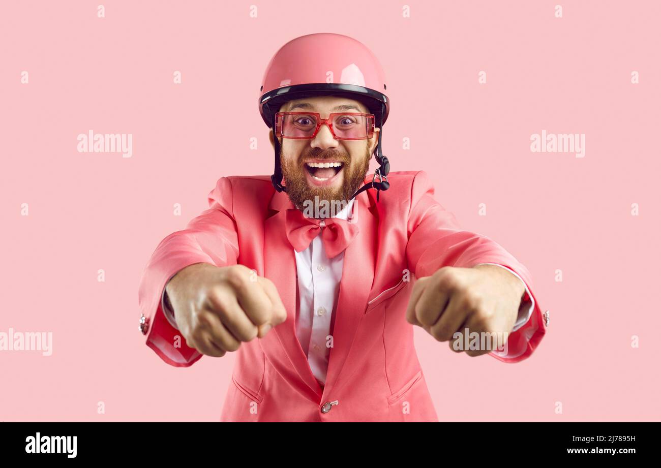 Lustiger Mann in rosa Schutzhelm gibt vor, Motorradfahrer isoliert auf rosa Hintergrund sein. Stockfoto
