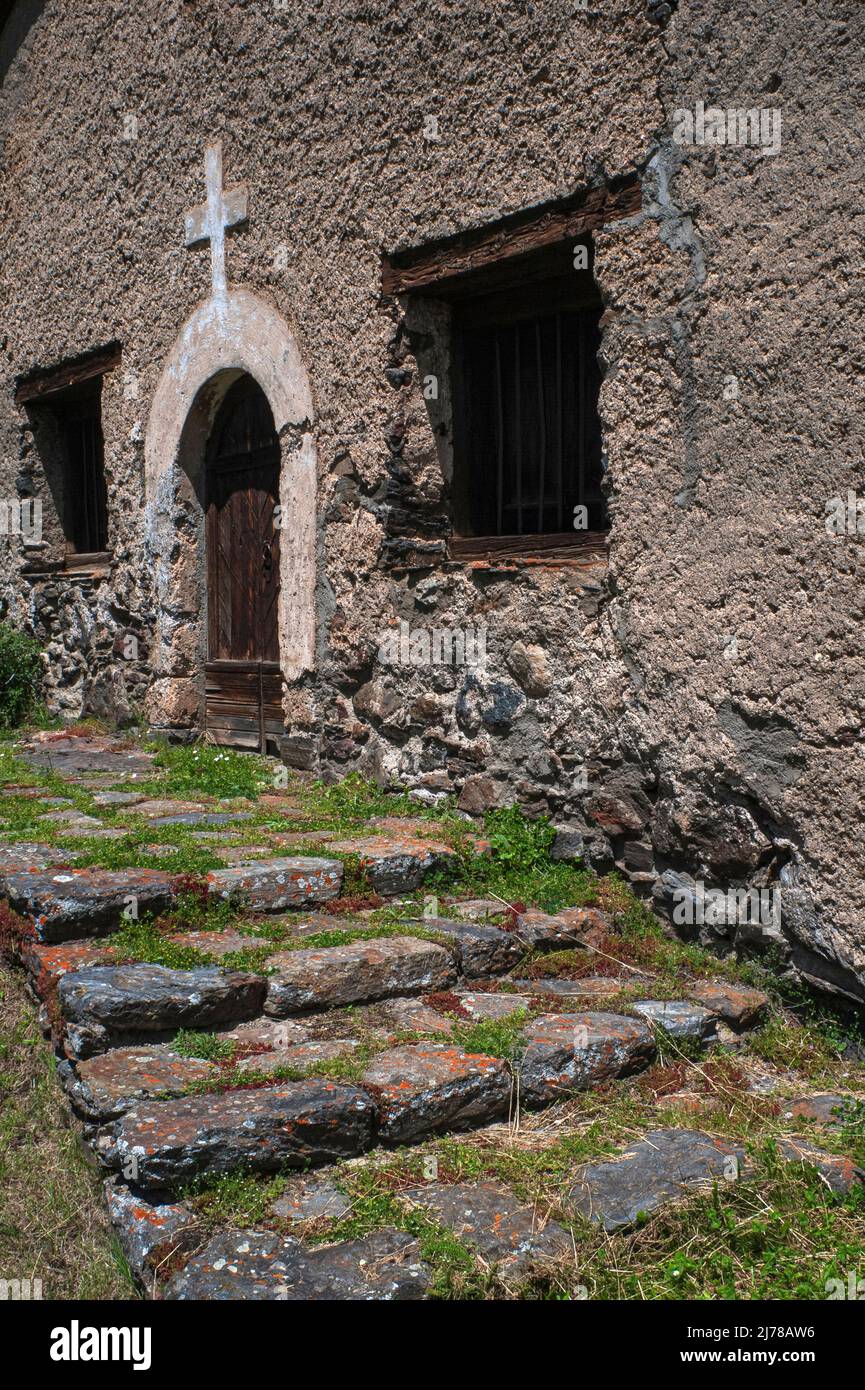 Orangefarbene Flechten stellen alte Stufen auf, die zur rustikalen Dorfkirche Sant Pere del Serrat aus dem frühen 16.. Jahrhundert in El Serrat im Ordino-Tal, Andorra, führen. Der rechteckige Innenraum verfügt über eine Holzgalerie und ein Ende 1500s oder Anfang 1600s bemaltes Altarbild, das dem heiligen Petrus gewidmet ist. Stockfoto