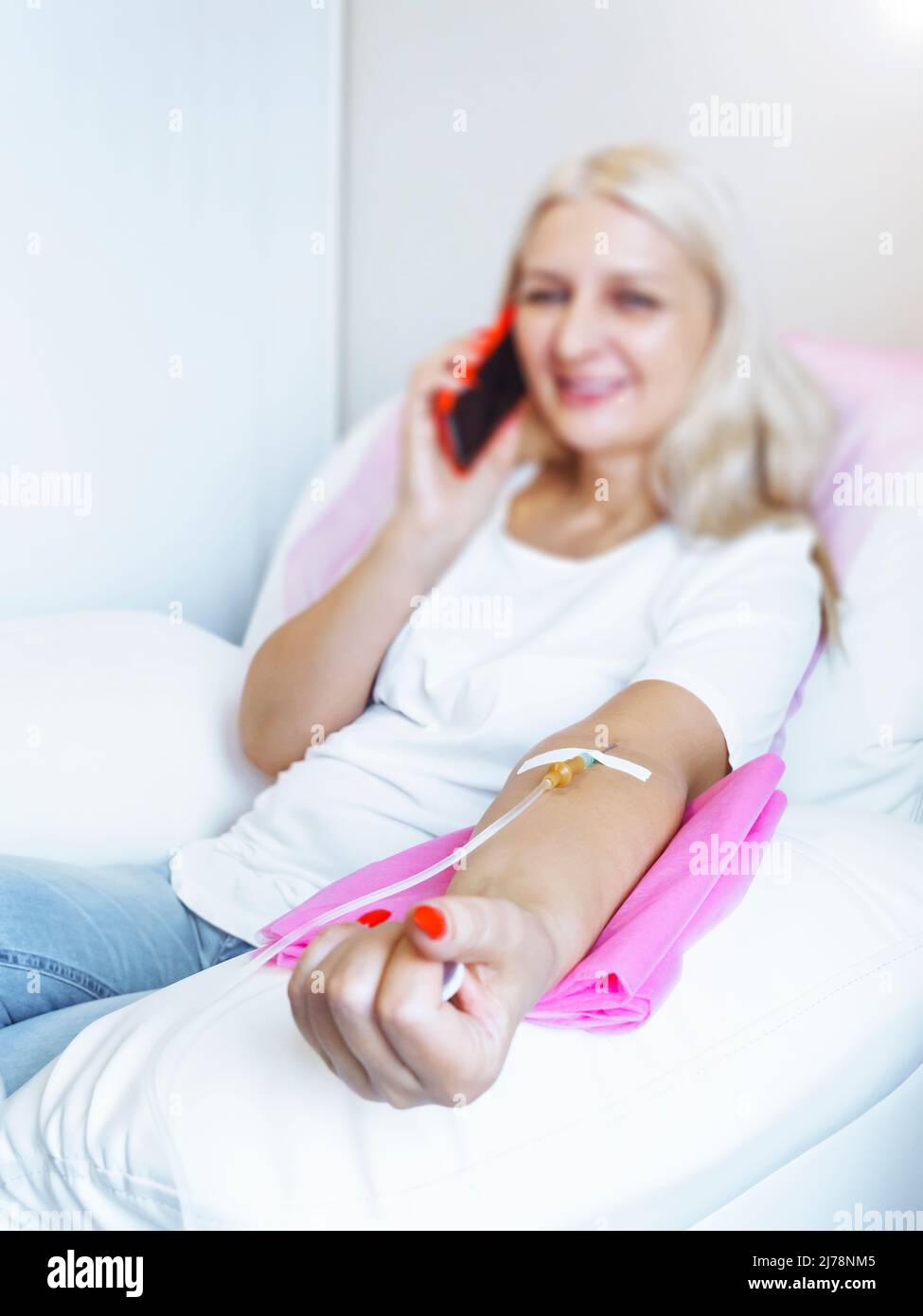 Frau im Krankenhaus spricht am Mobiltelefon, während die Nadel im Arm ist, Vitamin Therapy IV Drip Infusion im Frauenblut. Stockfoto