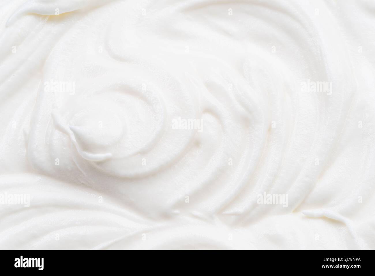 Cremige Wellen und Wirbel in Joghurt oder cremefarbener Oberfläche. Draufsicht. Stockfoto