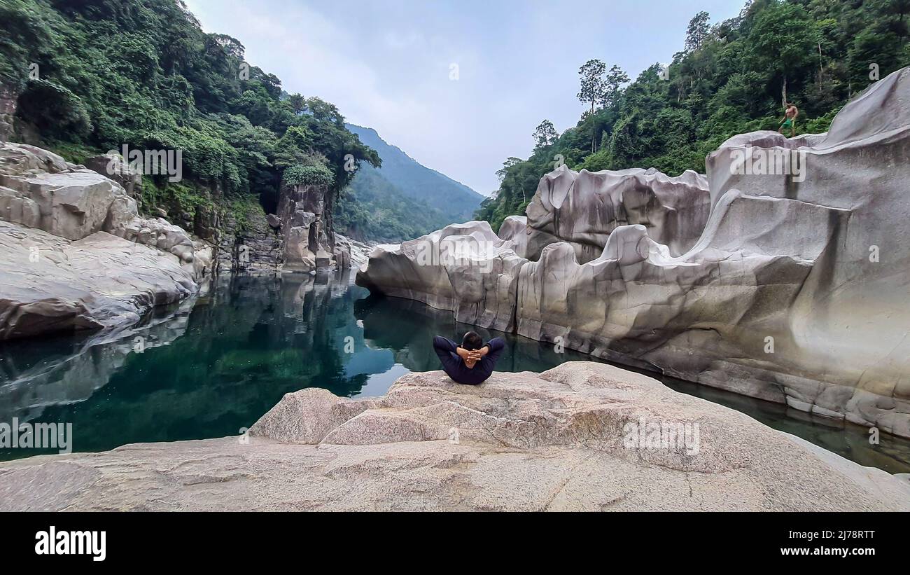 Isolierter junger Mann, der auf einem natürlich geformten weißen glänzenden Stein in einzigartiger Form am trockenen Flussbett sitzt, wird bei Sliang wah Umngot amkoi jaintia hi aufgenommen Stockfoto