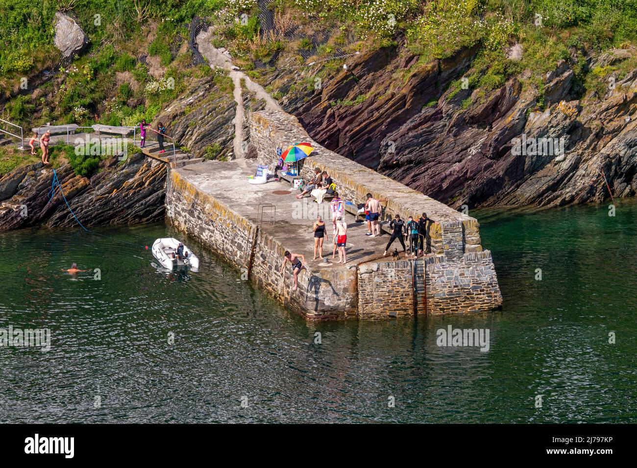 Menschen / Urlauber, die die heißen Juli-Bedingungen auf einem Steg in Polperro Harbour - Polperro, Cornwall, Großbritannien, genießen. Stockfoto