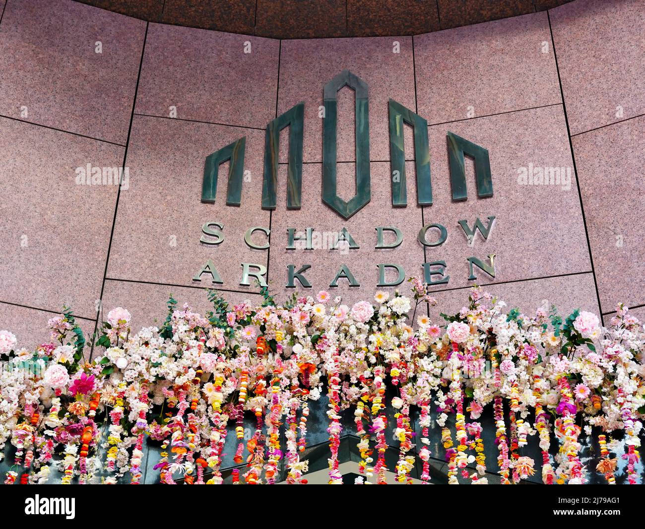 Eingangslogo des Einkaufszentrums „Schadow-Arkaden“ mit farbenfroher Frühlingsblumendekoration. Lage: Innenstadt Düsseldorf/Deutschland. Stockfoto