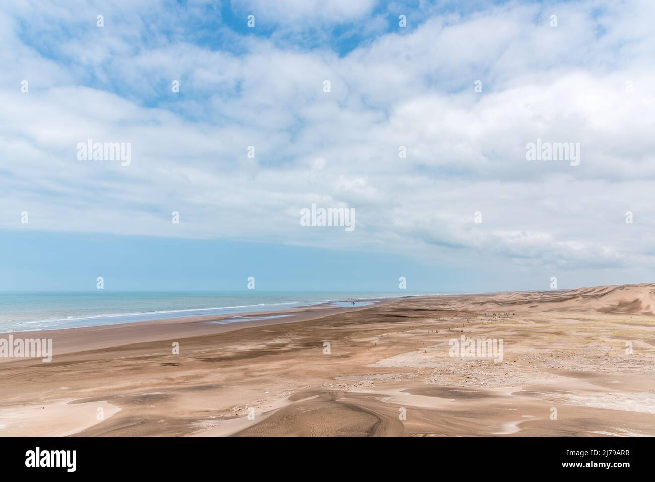 Panoramafoto des Sandes und der Dünen einer Wüste vor dem Meer mit einigen Wolken am Himmel Stockfoto