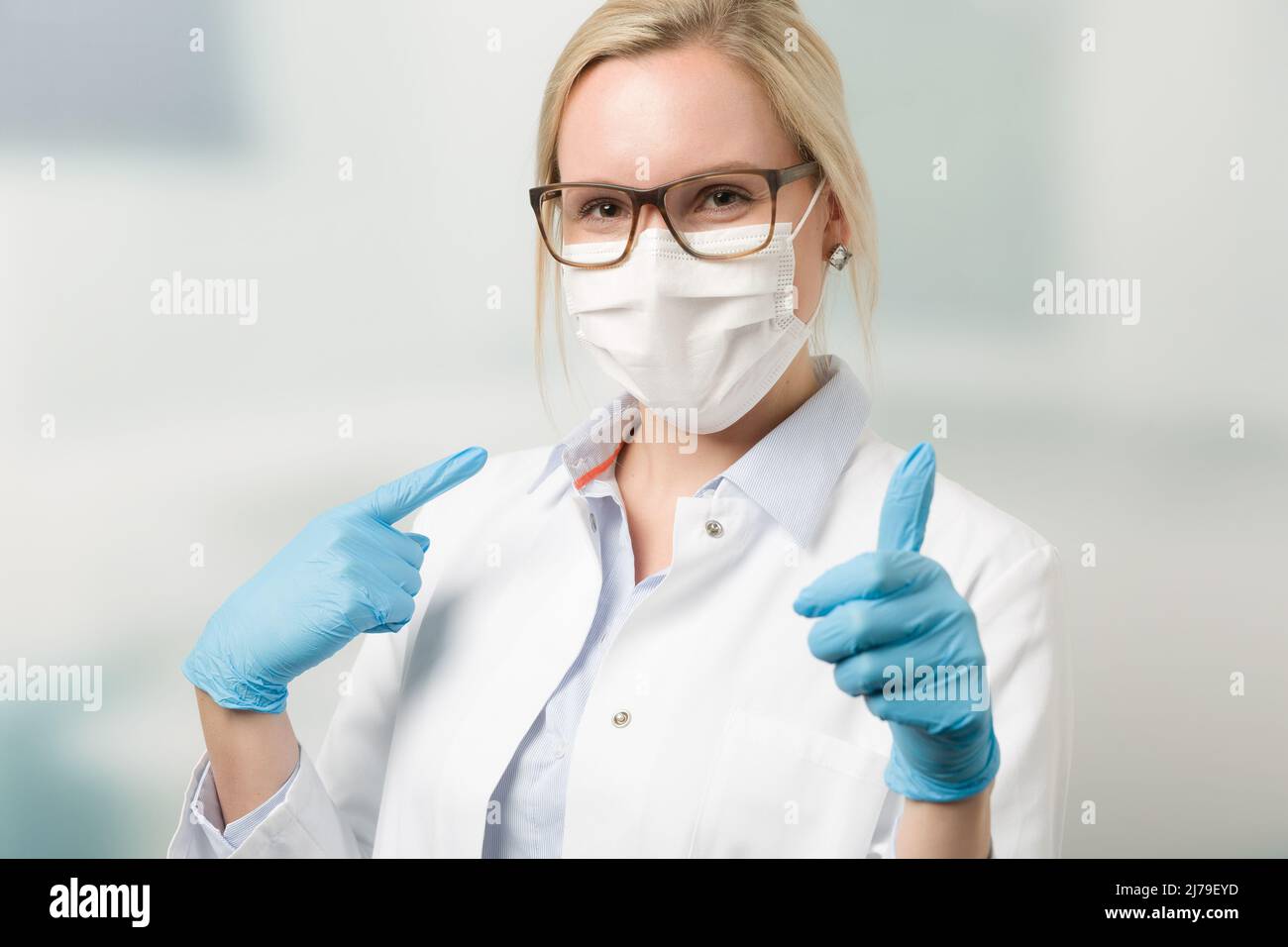 Ärztin mit medizinischer Gesichtsmaske und medizinischen Handschuhen zeigt Daumen nach oben Stockfoto