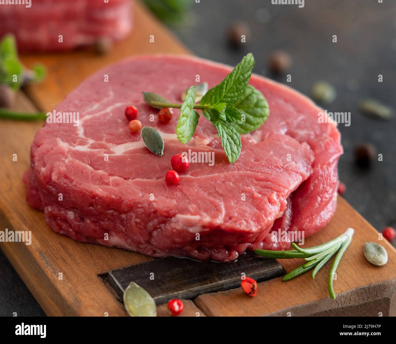 Rohe Rinderfiletsteaks auf Holzbrett auf dunklem Hintergrund Nahaufnahme. Portionierte Filet-Mignons mit Gewürzen und Kräutern. Konzept der Sommerkost Stockfoto