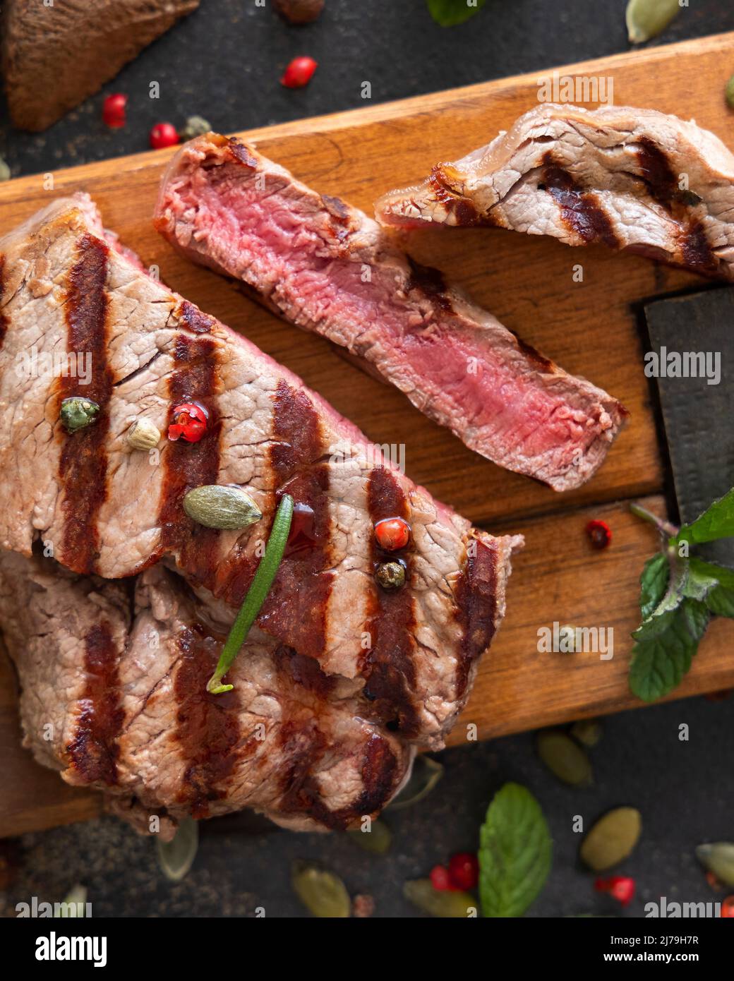 Gegrillte Rinderfilet-Steaks auf dunklem Tisch, Nahaufnahme von oben. Portioniertes Filet Mignon mit Gewürzen und Kräutern. Konzept der Sommerkost, Fleischesser. Stockfoto