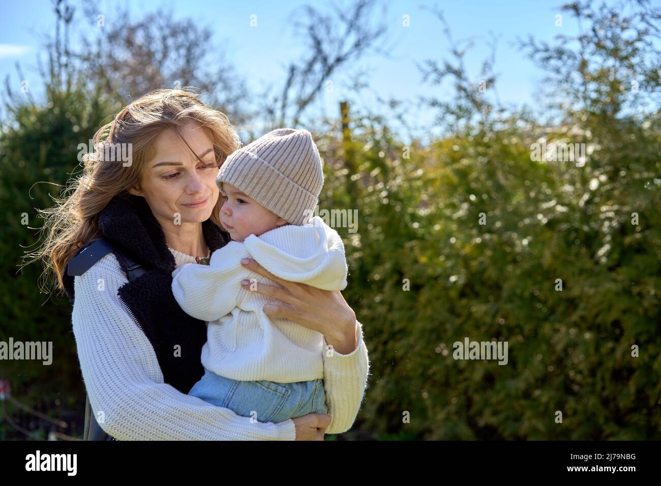Mutter hält ihre Tochter an den Händen und blickt sie mit Liebe und Lächeln  an. Baby in der Mütze und im Hoodie Stockfotografie - Alamy