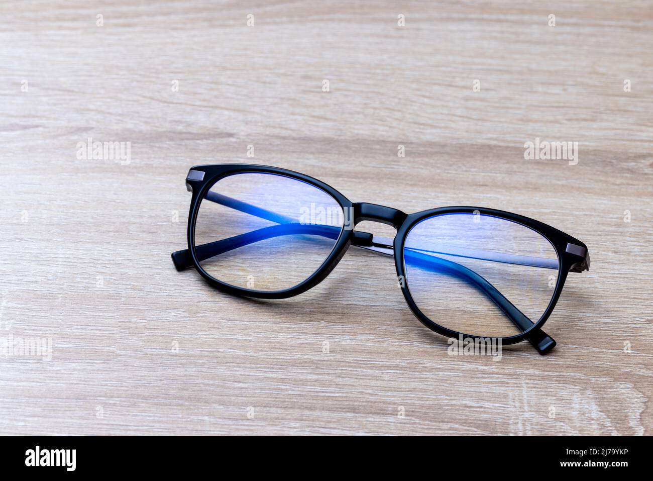 Klassische schwarze Lesebrille auf Holztisch. Eine Brille mit Filterbeschichtung blockiert das blaue Licht des Bildschirms, um das Computer Vision Syndrom zu verhindern. Stockfoto