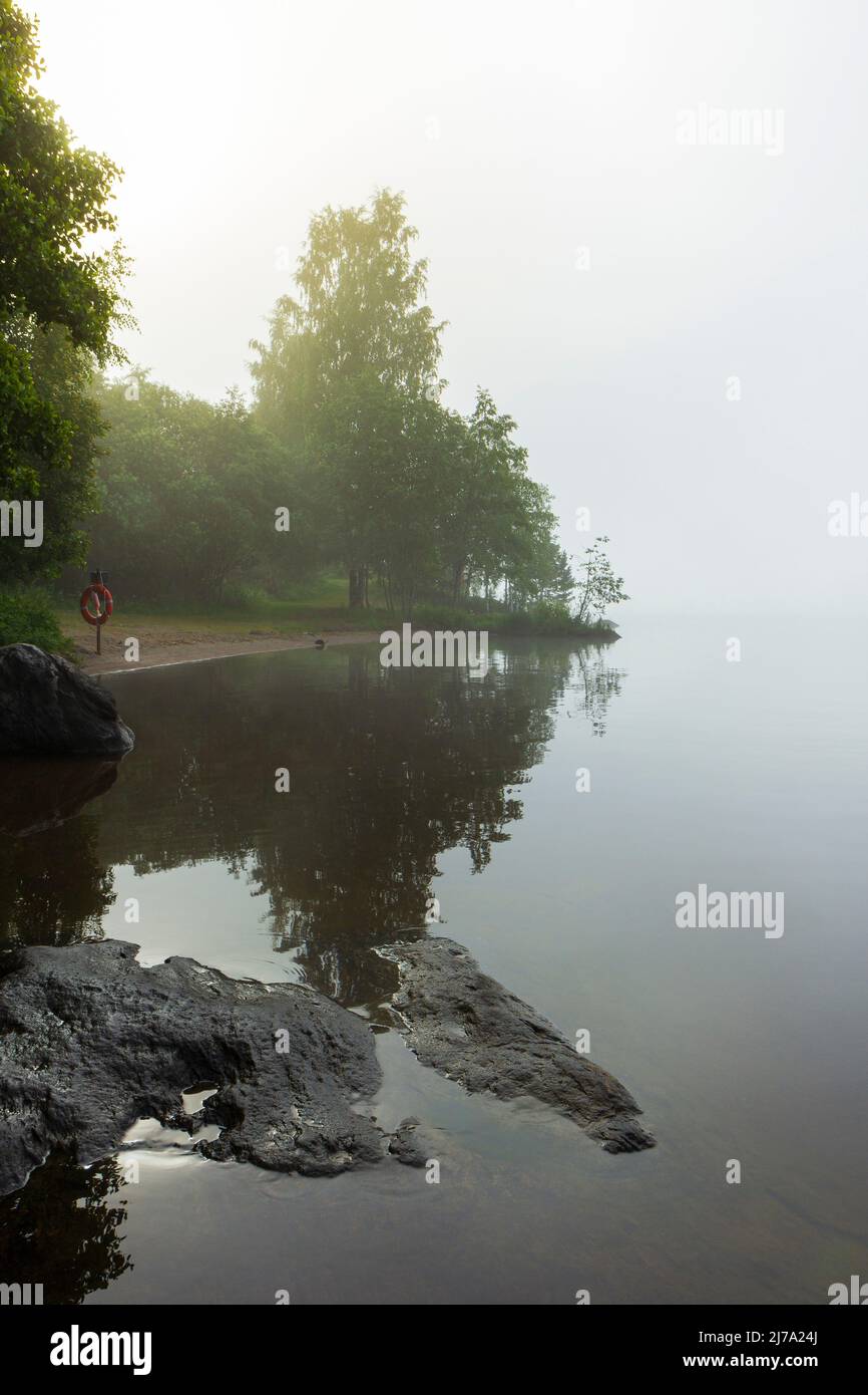 Ruhiger, ruhiger und nebliger See und Spiegelung der Bäume in Finnland am Morgen im Sommer. Stockfoto