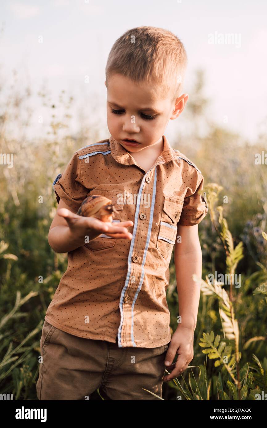 Ein kleines Kind hält eine Schnecke in den Händen und untersucht sie sorgfältig Stockfoto