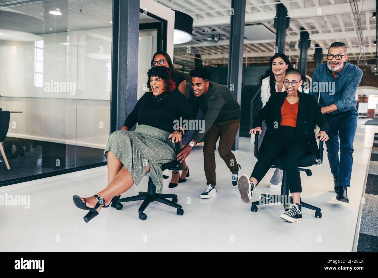 Spaß während der Geschäftszeiten. Ein fröhliches Team von Geschäftsleuten, die sich in einem modernen Büro auf Stühlen schieben. Glückliche Geschäftskollegen, die Spaß haben und c Stockfoto