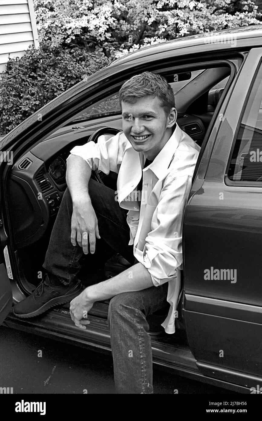Schöner junger Mann mit riesigem Lächeln von seinem grauen Auto Stockfoto