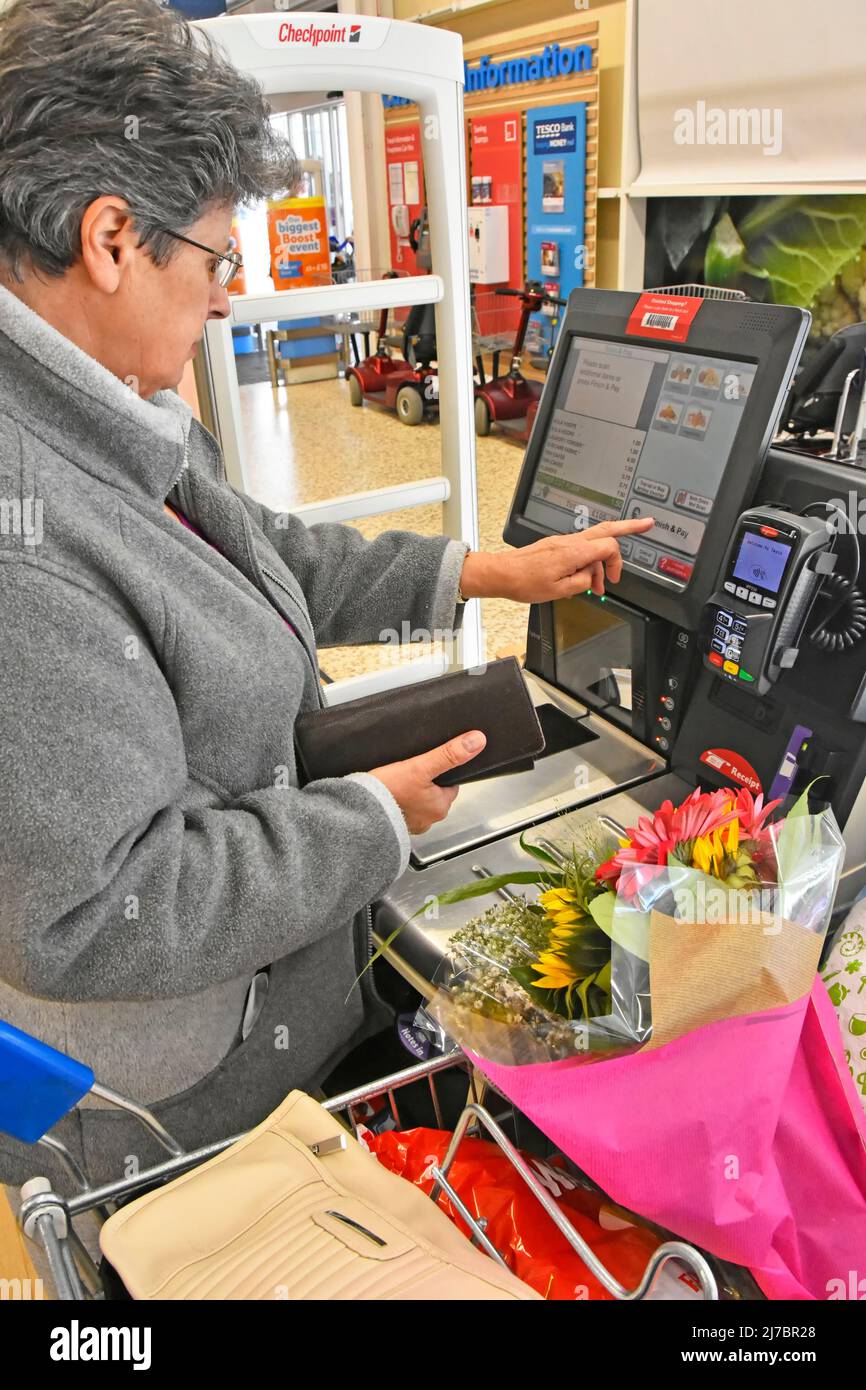 Frau hält Geldbeutel einkaufen Tesco Self-Service Check-out-Scan, wie Sie einkaufen, bis die Zahlung per Debit-Karte neben vollen wöchentlichen Lebensmittelgeschäft Trolley England Großbritannien Stockfoto