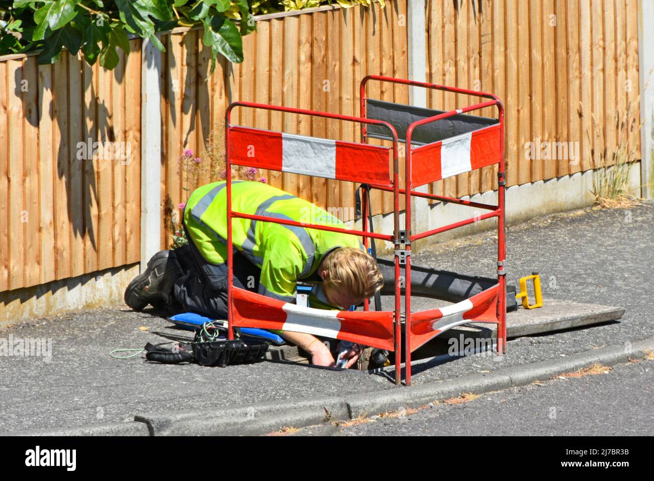 Openreach Telefoningenieur in Sichtjacke bei der Arbeit auf den Knien, die sich über und Kopf nach unten schachteln, bei der Reparatur des Telefonkabels UK Stockfoto