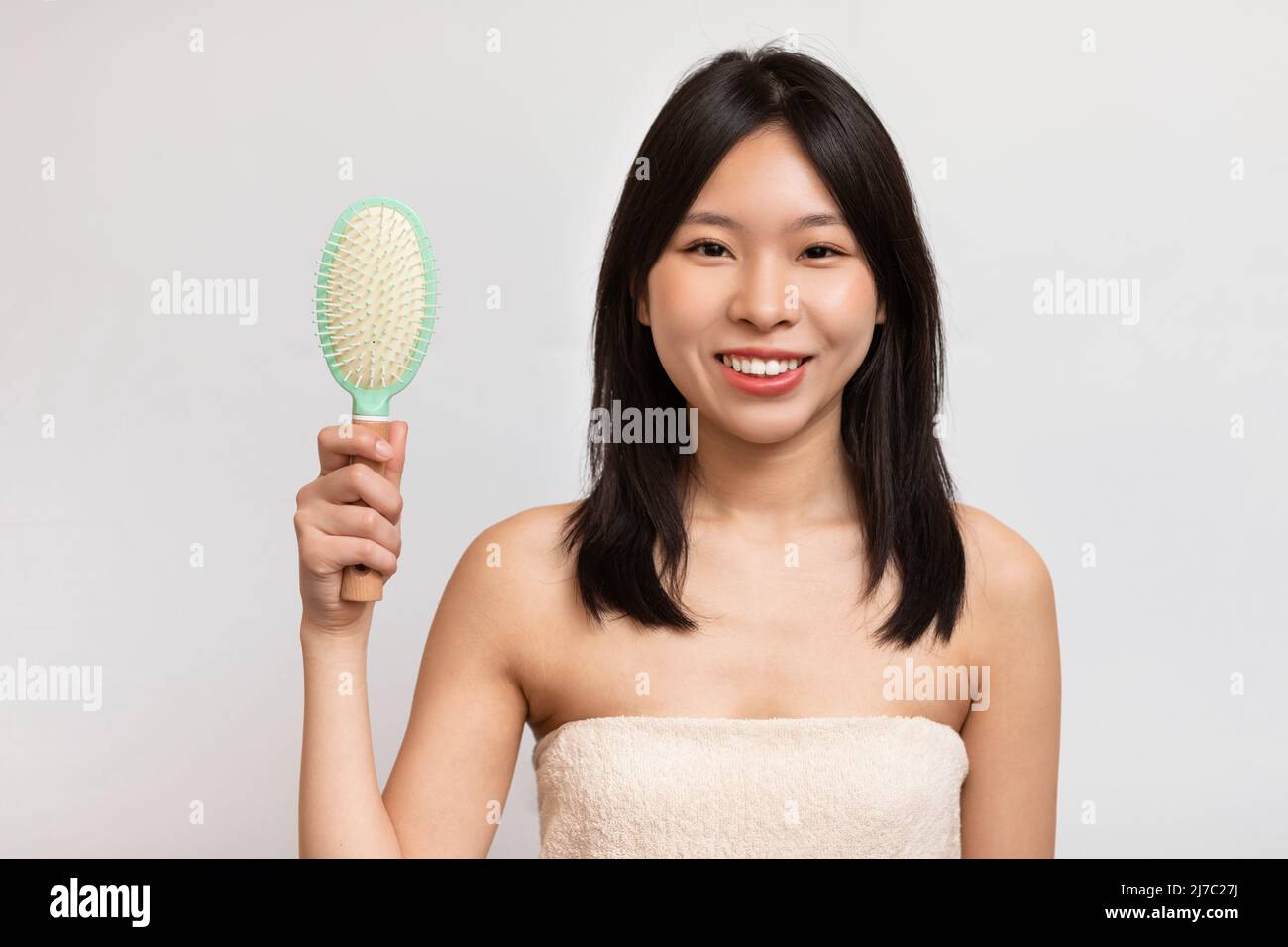 Porträt einer fröhlichen asiatischen Frau, die sich die Haare putzt Stockfoto