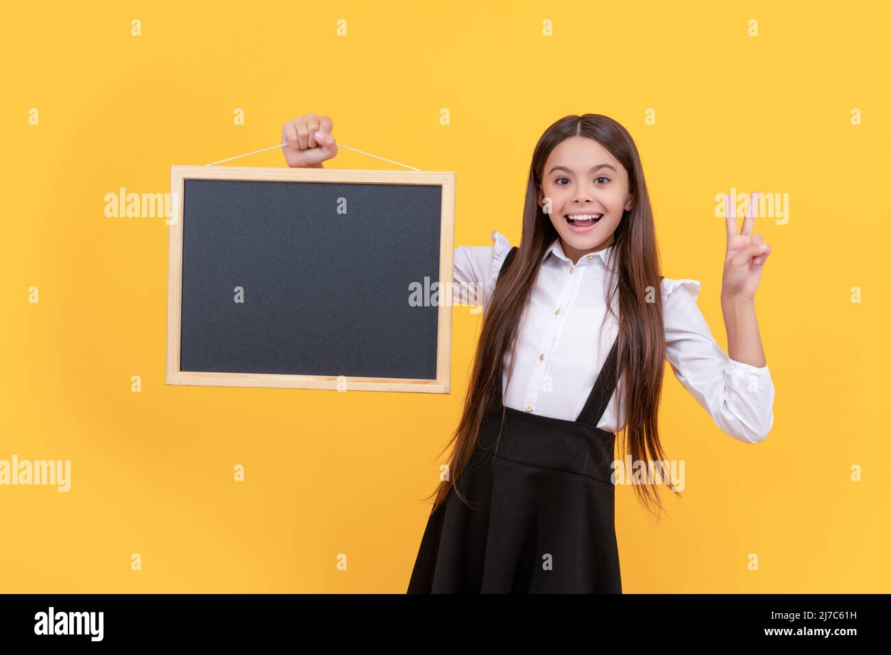 Lächelndes Teenager-Mädchen in Uniform halten Schule Tafel für Kopie Raum zeigt Frieden, Schulverkauf. Stockfoto