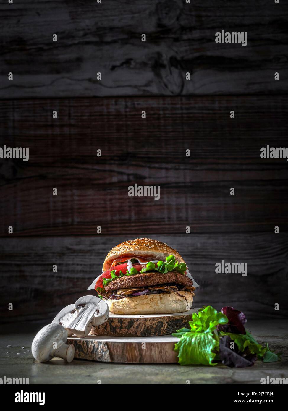 Hamburger mit Kichererbsen-Patty, Tomaten, Pilzen und Gemüse auf Roggenbrot. Herum, Pilze und Salat. Speicherplatz kopieren. Vertikale Aufnahme Stockfoto