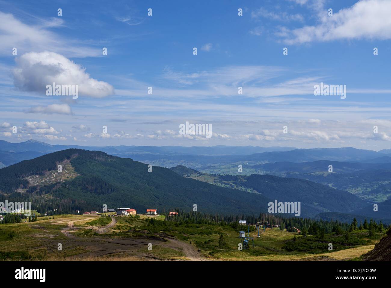 Gemütliches Dorf in den Bergen, mit ländlicher Straße auf Hochland Feld. Luftaufnahme der Bergsiedlung, mit kleinen Häusern und Gebäuden im Sommer, mit Berglandschaft im Hintergrund. Konzept von Hochland. Stockfoto