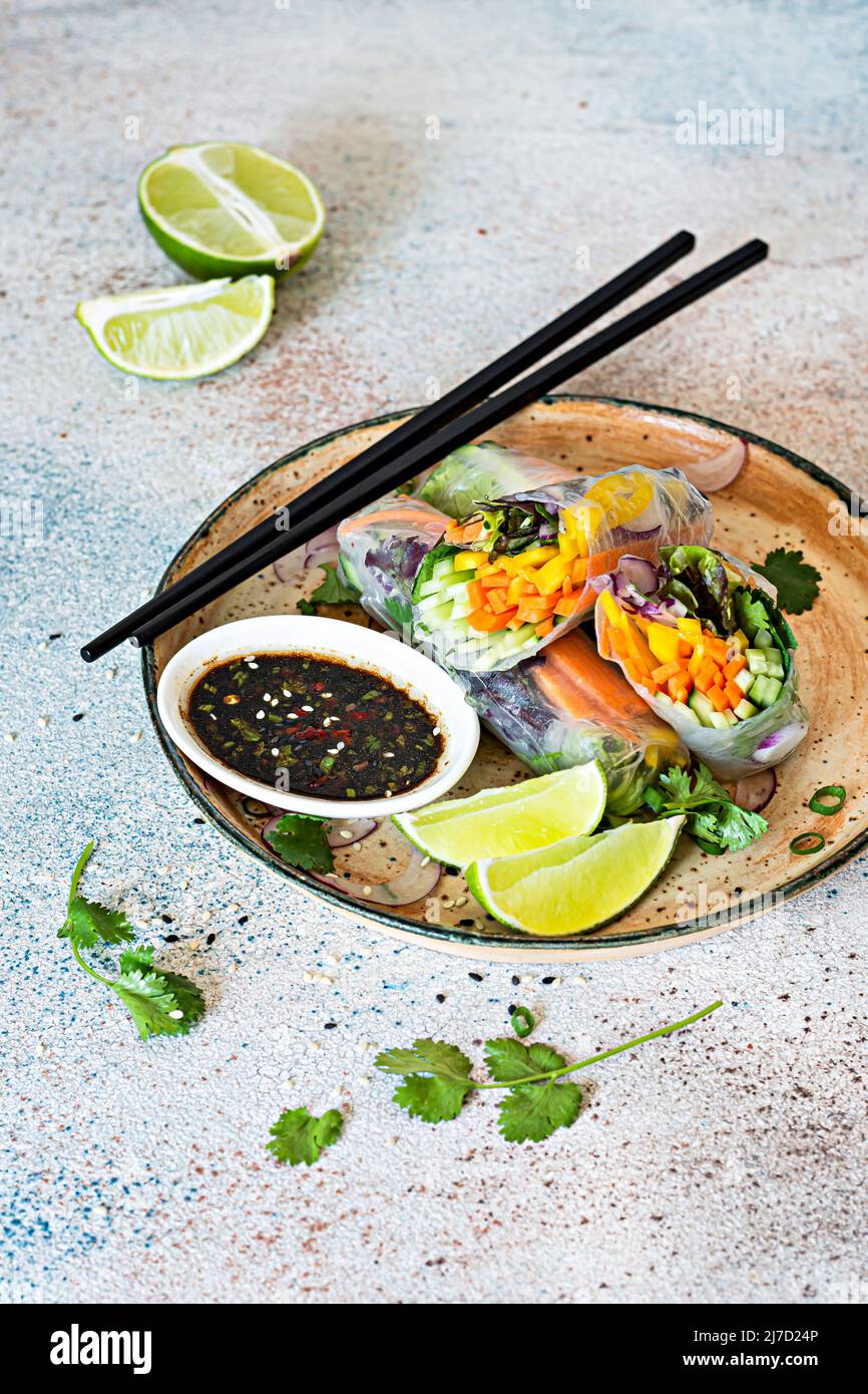 Frische asiatische Vorspeise Frühlingsrollen (Nem) aus Reispapier und rohem Gemüse und Kräutern mit heißer Sauce auf hellblauem Hintergrund. Vietnamesische Küche Stockfoto