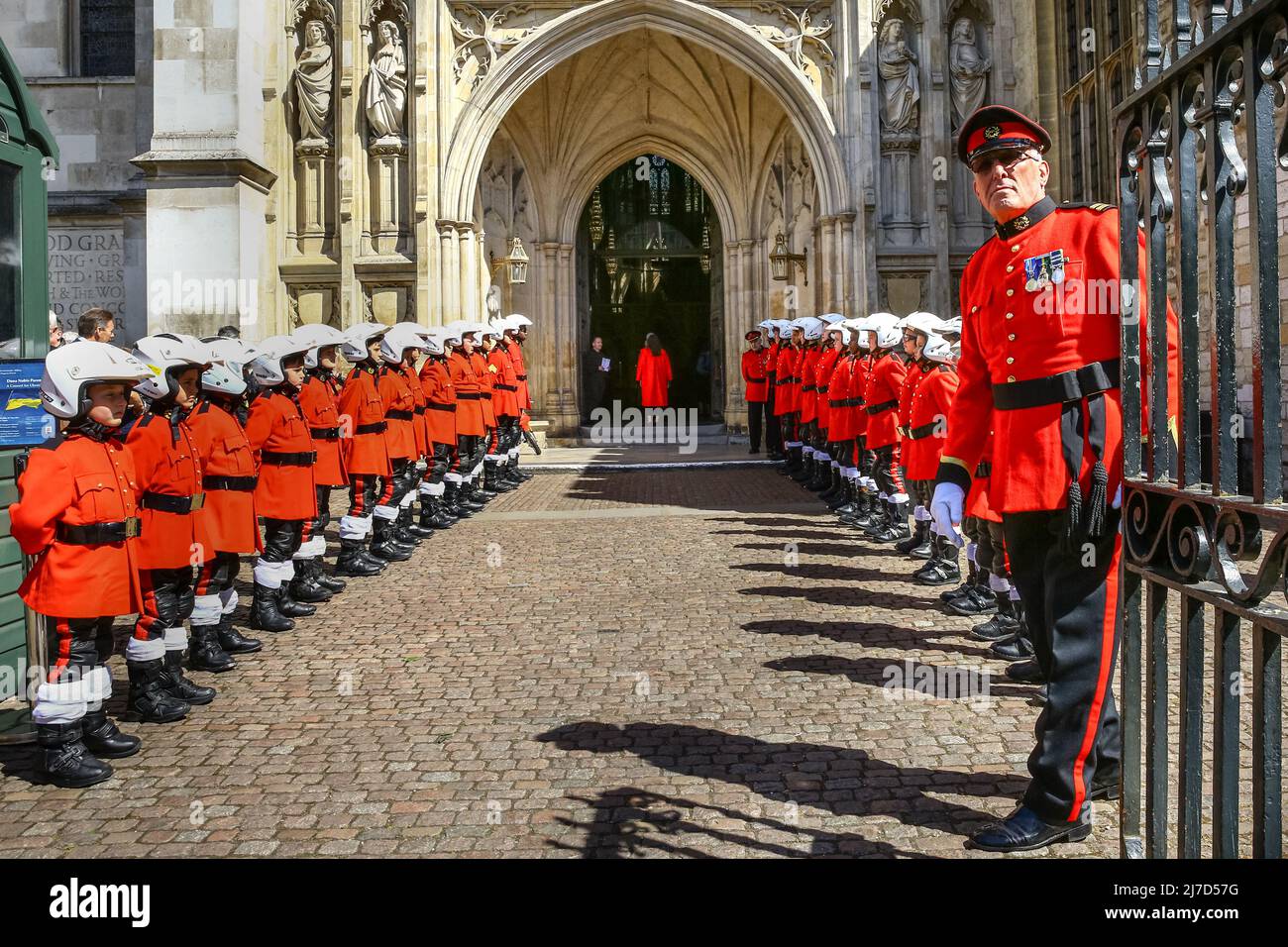 London, Großbritannien, 8.. Mai 2022. Kinder in farbenfrohen roten „Biker“-Uniformen und Helm säumen den Eingang der Westminster Abbey, während Mitglieder des Clubs zu einem langen Service und Segnung von Fahrrädern eintreten. Der 59 Motorcycle Club wurde von Reverend John Oates als Jugendclub in der Eton Mission, Hackney Wick, gegründet und wuchs später 1962 vom Ace Cafe in London aus, feiert heute seinen 60.. Geburtstag mit einem Gottesdienst in der Westminster Abbey in Westminster. Viele der Vereinsmitglieder sind mit ihren Fahrrädern unter der Verantwortung von Pater Sergiy Diduk angekommen. Stockfoto