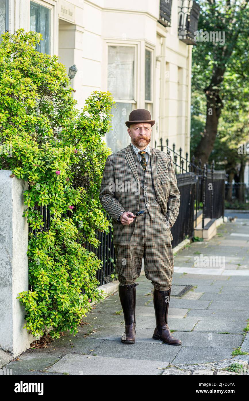 Gut gekleideter englischer Gentleman mit Melone-Hut, der in der Straße mit einer Pfeife steht. Stockfoto