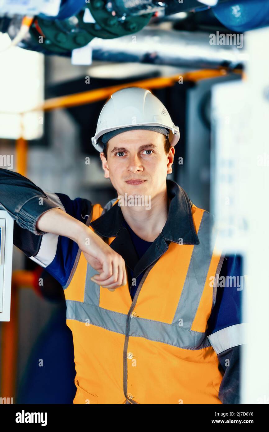 Porträt eines jungen kaukasischen Ingenieurs in weißem Helm und Schutzweste. Mitarbeiter der Gasindustrie in der Produktionsanlage.reale Szene. Stockfoto