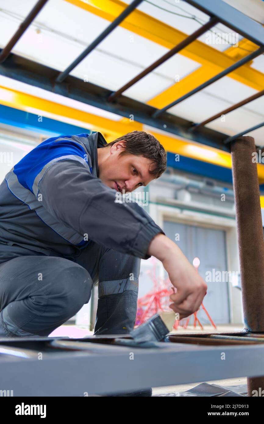 Maler von 30-40 Jahren kaukasischen Aussehen malt Metallstruktur in der Produktionshalle mit Pinsel. Echter Workflow. Stockfoto