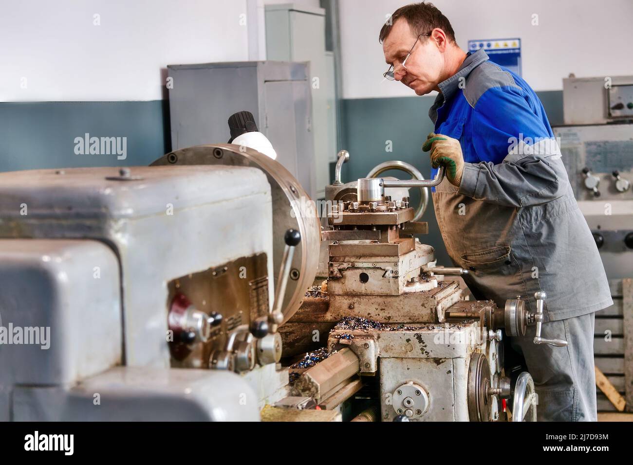 Turner in Overalls arbeitet hinter der Drehbank in der Produktionshalle. Verarbeitung von Metallprodukten. Industrieller Hintergrund. Stockfoto