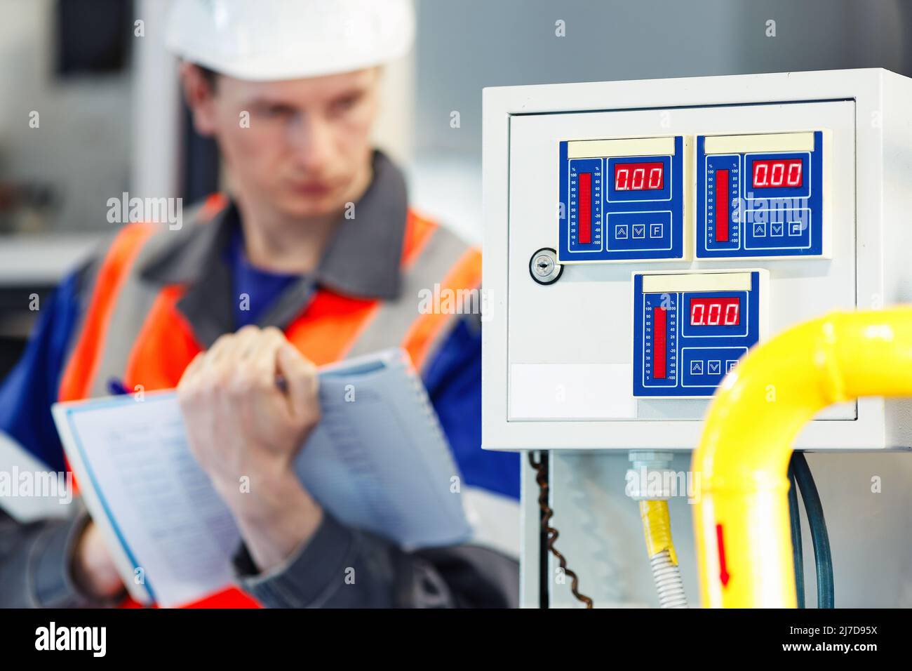 Der junge Ingenieur, der Helm und Schutzweste verwendet, zeichnet die Messwerte der Geräte oder des Gasverbrauchs im Kesselraum auf. Beginn der Heizperiode und Gasversorgung. Stockfoto
