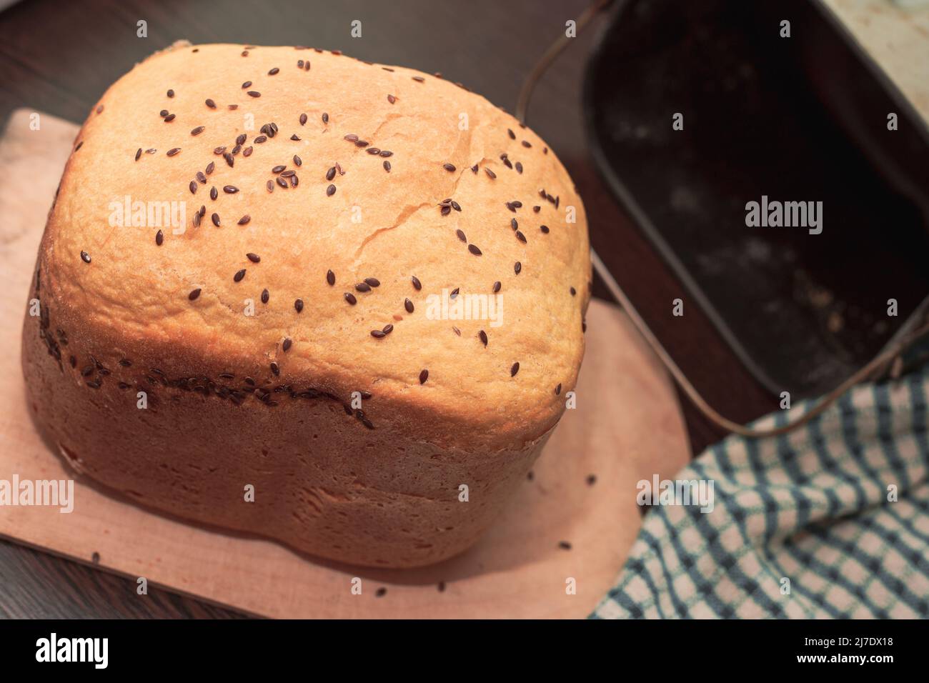 Frisches, selbstgebackenes Brot, bestreut mit Flachs- und Sesamsamen, in einer Brotmaschine gebacken. Köstliches hausgemachtes Gebäck. Stockfoto