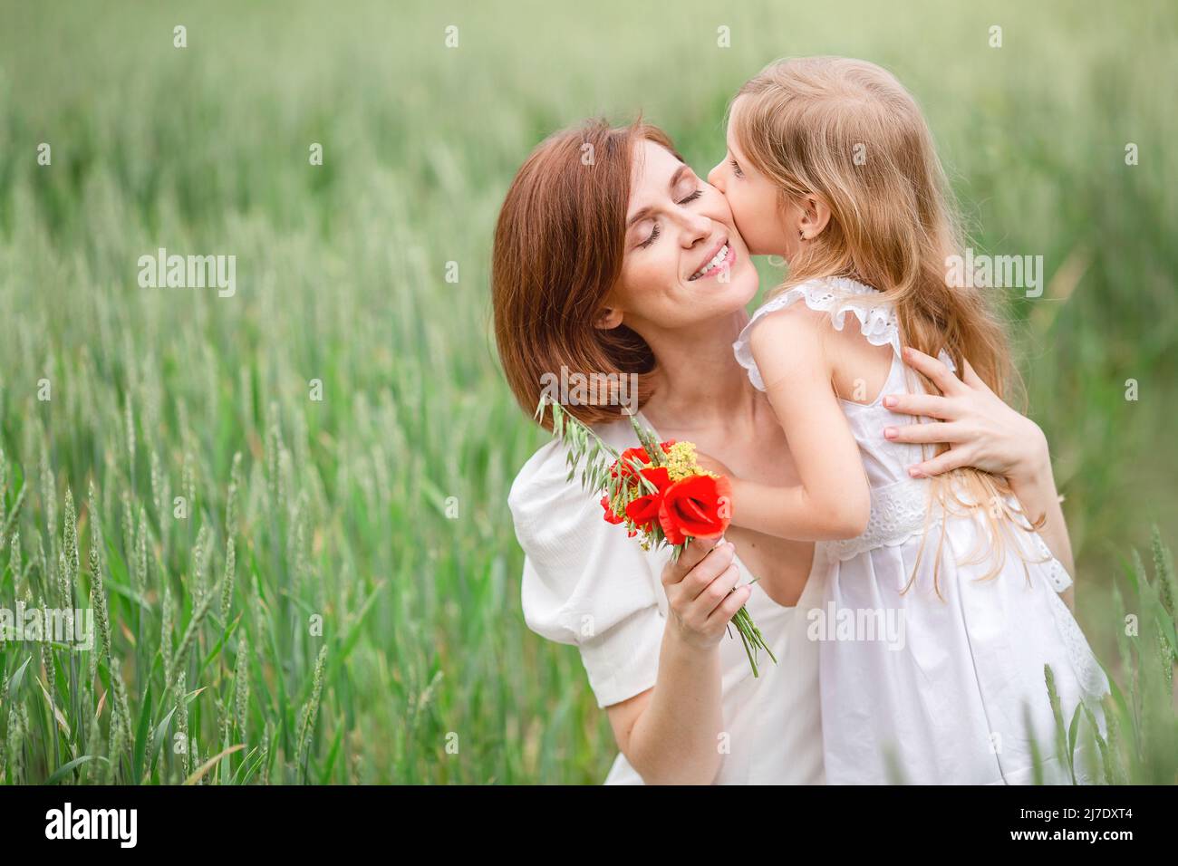 Mutter und Tochter gehen auf dem Feld. Ein blondes Mädchen mit langen Haaren gibt ihrer Mutter einen Strauß Mohnblumen für den Muttertag. Stockfoto