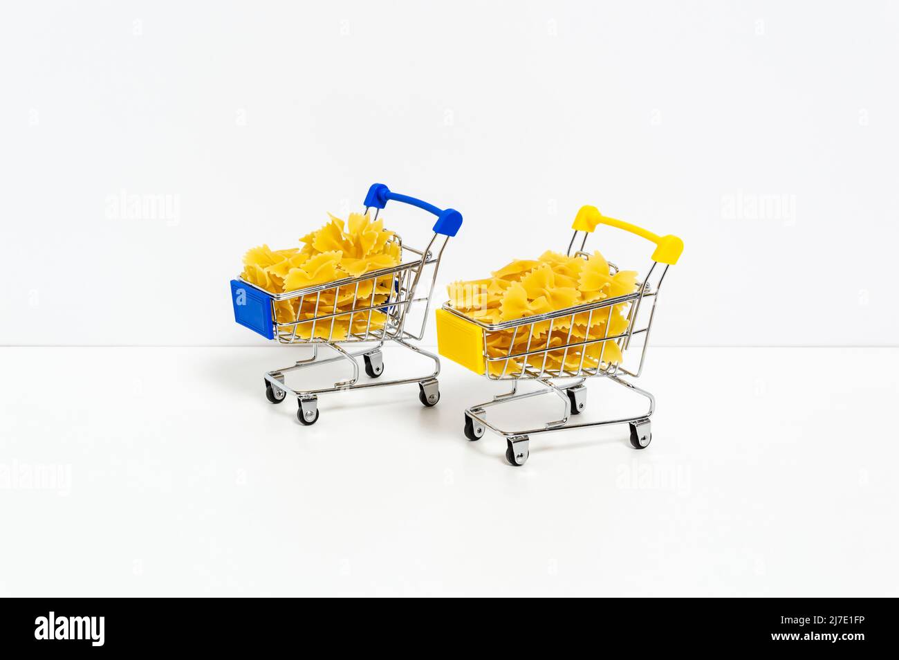 Ungekochte Farfalle Pasta in blauen und gelben Einkaufswagen in den Farben der ukrainischen Flagge isoliert auf weißem Hintergrund. Nahrungsmittelkrise, Preiserhöhung Stockfoto