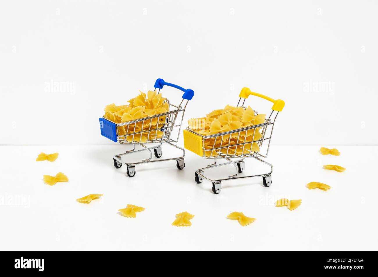 Ungekochte Farfalle Pasta in blauen und gelben Einkaufswagen in den Farben der ukrainischen Flagge isoliert auf weißem Hintergrund. Nahrungsmittelkrise, Preiserhöhung Stockfoto