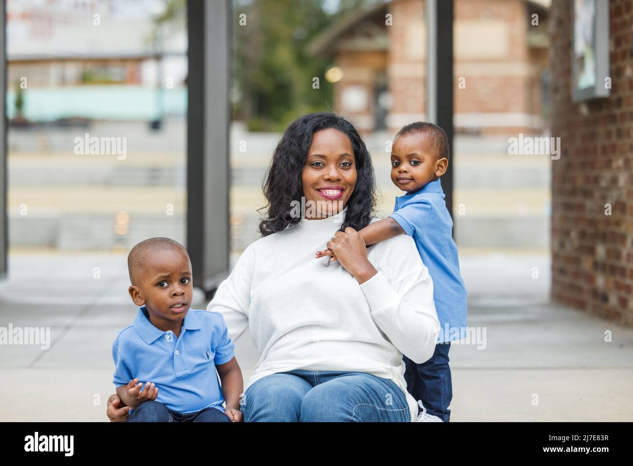 Eine Mutter mit langen Haaren sitzt draußen mit ihren beiden kleinen Söhnen Stockfoto