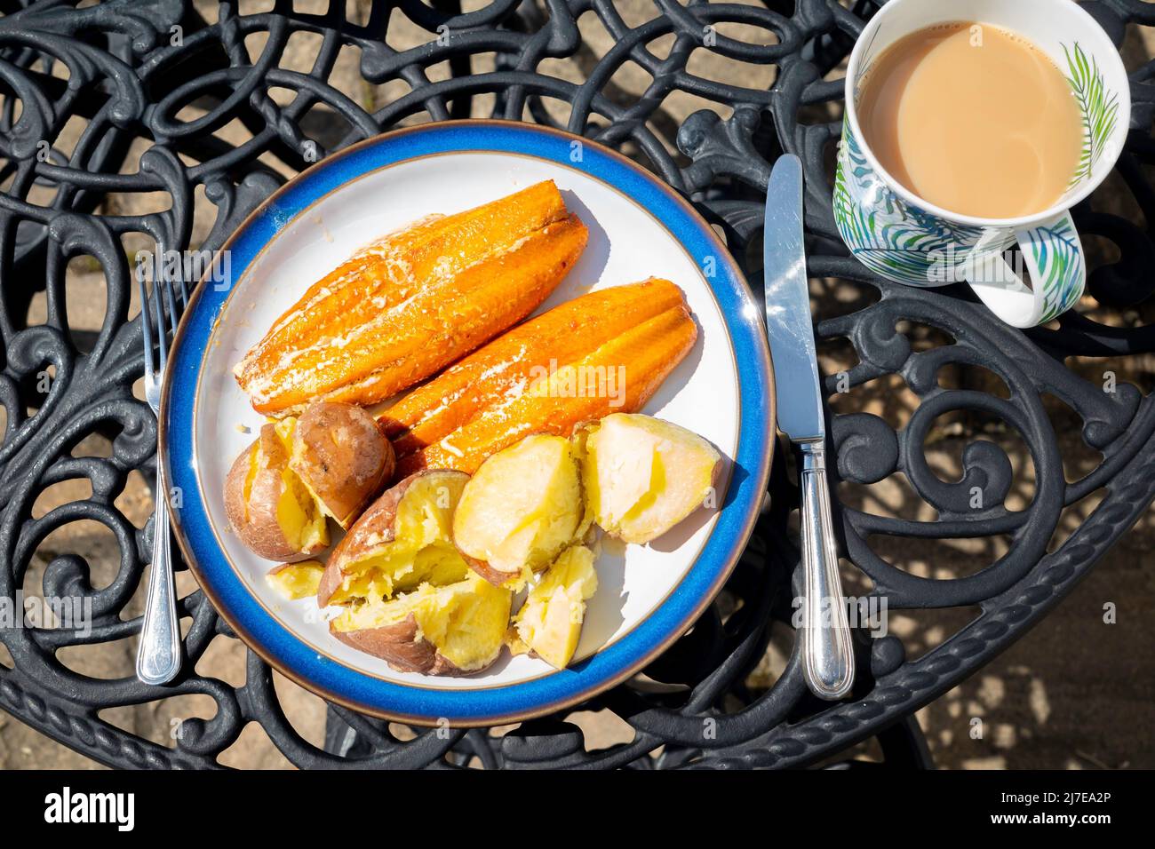 Mittags zwei saftige Kipper mit gebackenen Kartoffeln auf einem Tisch im Freien mit einer Tasse Tee Stockfoto