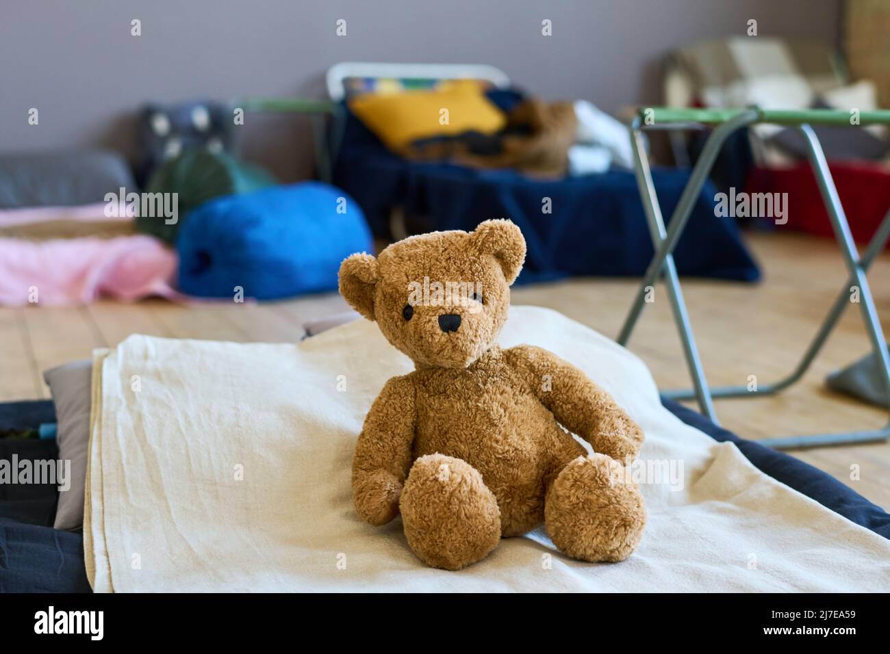 Teddybär von brauner Farbe sitzt auf dem Bett mit weißer Baumwolldecke Flüchtlingskind in großen Raum für Migranten vorbereitet gemacht Stockfoto