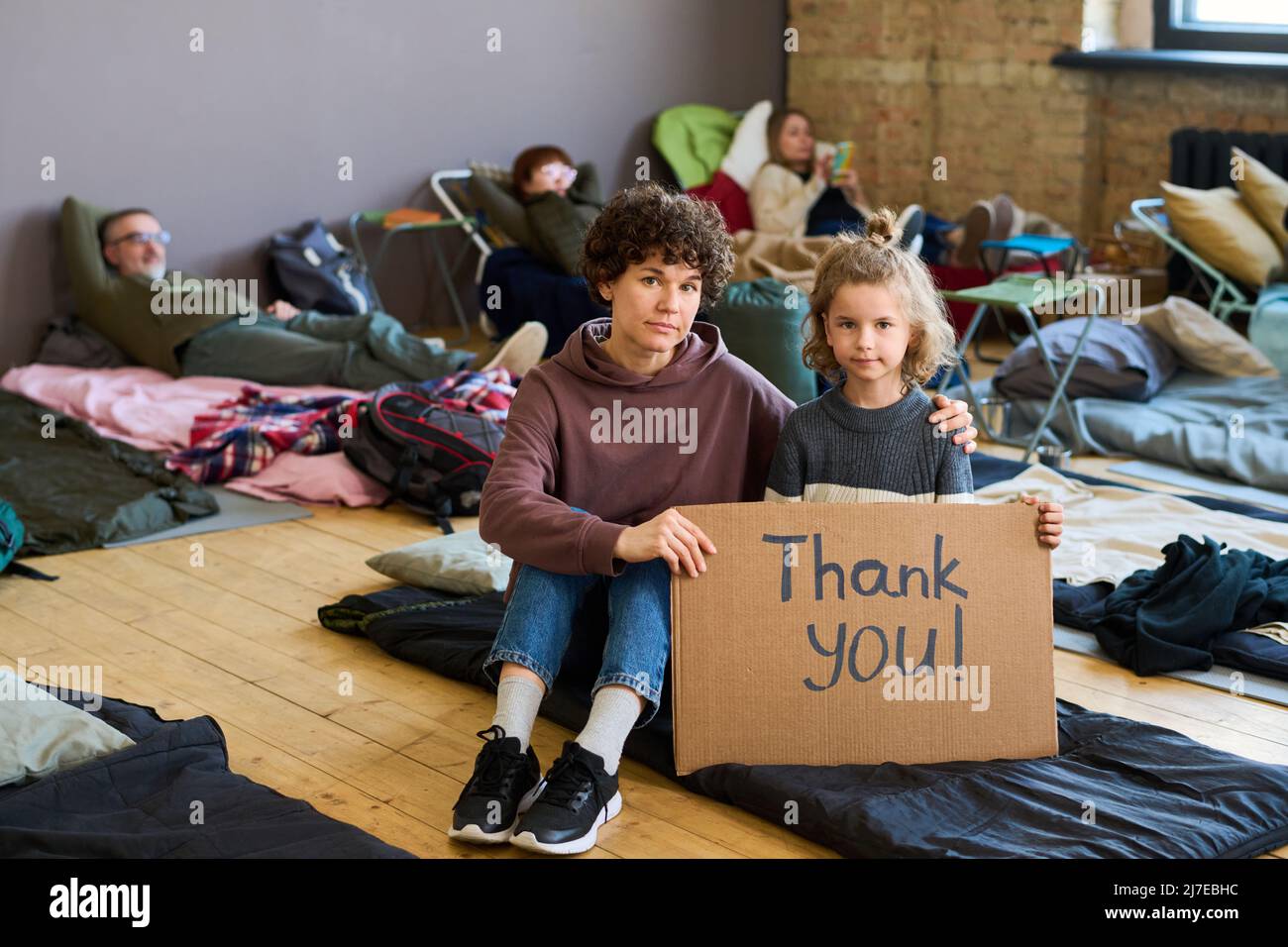 Die junge, dankbare Frau und ihr kleiner Sohn drückten ihre Dankbarkeit den Freiwilligen aus, während sie auf dem Schlafplatz auf dem Boden des Lagers saßen Stockfoto