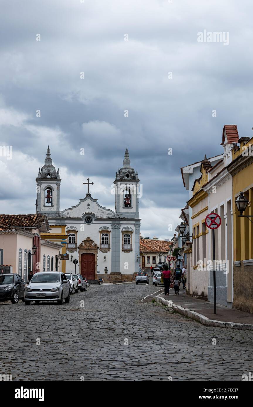 Getulio Vargas gepflasterte Straße mit Kolonialhäusern auf beiden Seiten und die große Kirche Nossa Senhora do Rosario auf der Rückseite unter bewölktem Himmel. Stockfoto