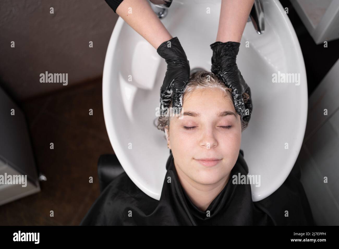 Nahaufnahme der Hände des Friseurs in Handschuhen, die den Kopf eines Kunden waschen. Schöne Dame entspannen und fühlen sich wohl beim Waschen der Haare mit Shampoo und Stockfoto