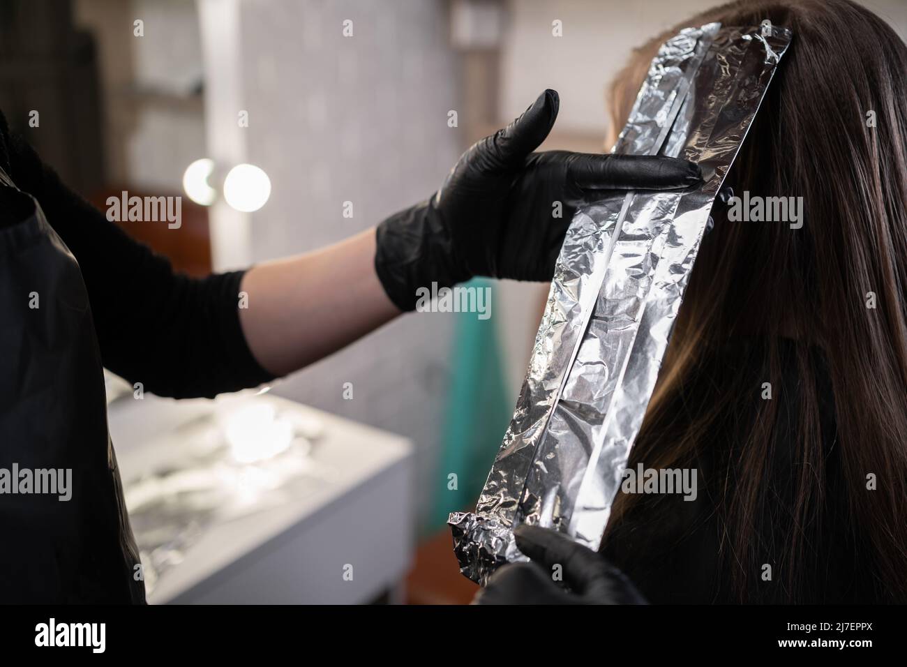 Nahaufnahme der Hände des Friseurs Verstecken Haarsträhnen der schönen jungen Frau mit Aluminiumfolie durch Ändern der Haarfarbe Stockfoto