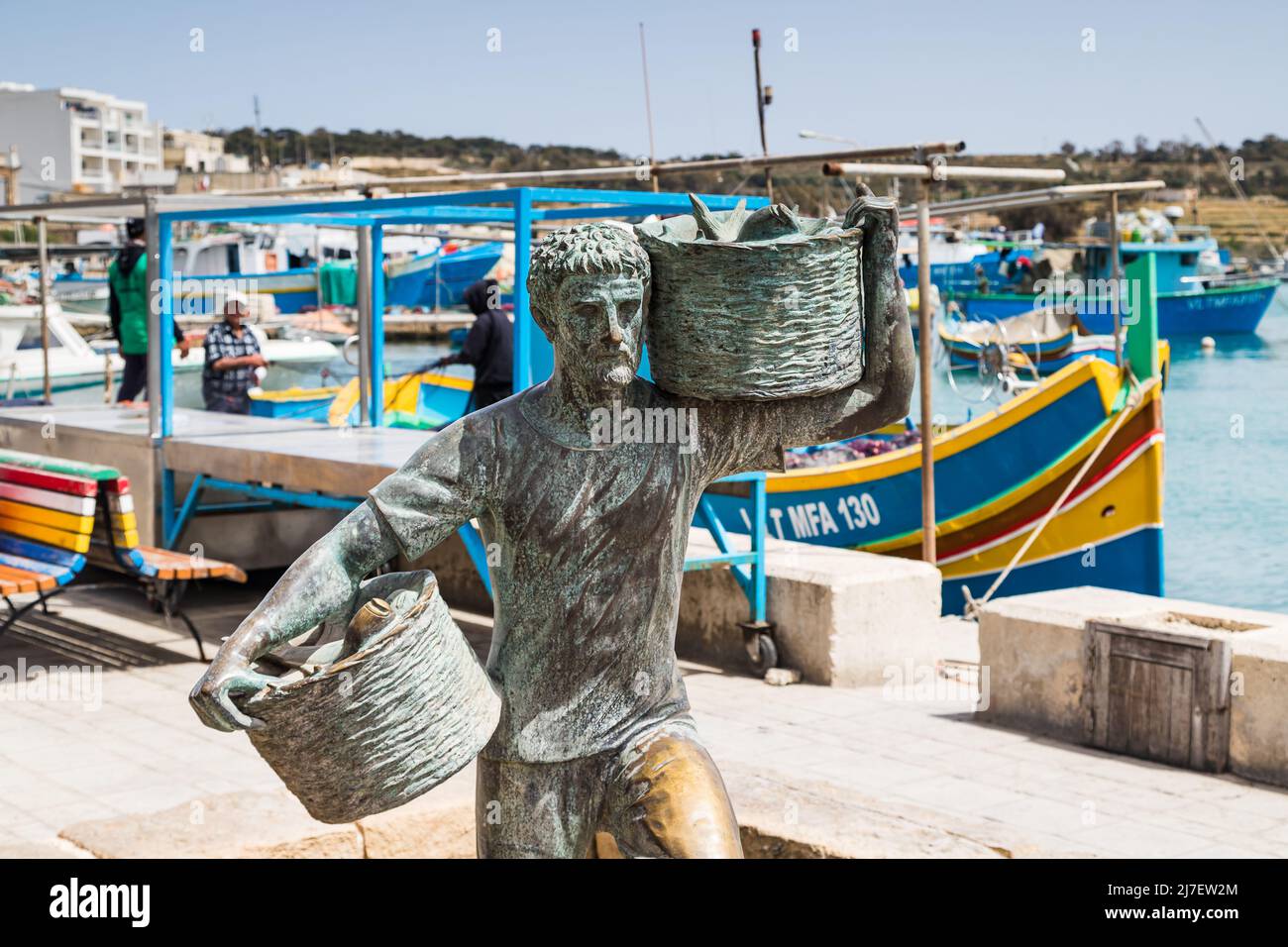 Fischerstatue im Hafen von Marsaxlokk gesehen in Malta im April 2022 mit zwei Körben Fisch aus einem Boot. Stockfoto